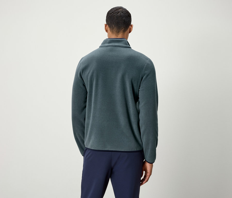 Muž zády k fotoaparátu má na sobě zelenou fleecovou bundu a modré kalhoty.