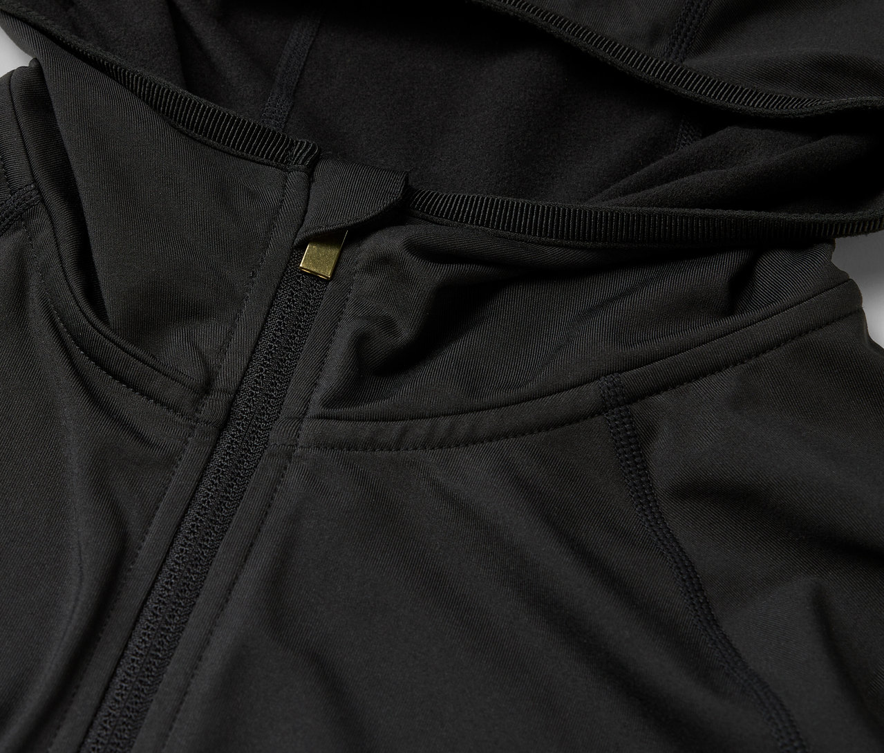 Detail černé mikiny s kapucí a zipem.