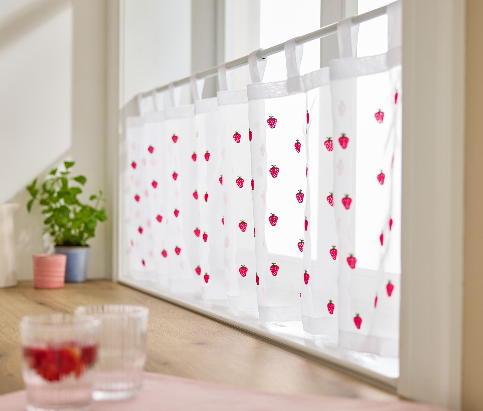 V okně visí vyšívaná krátká záclona s motivem jahod.
