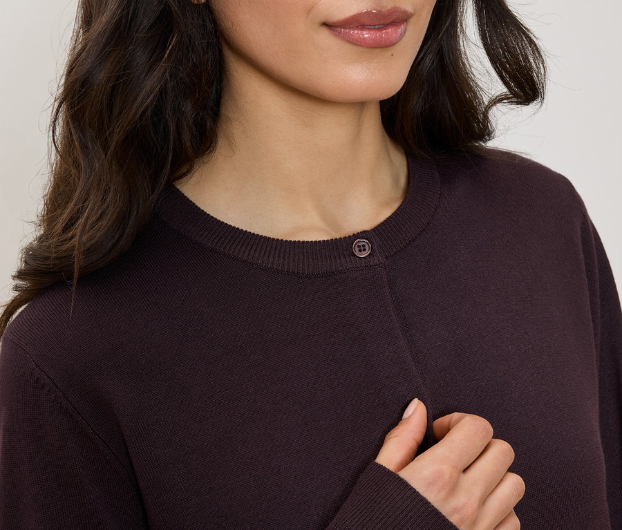 Horní část těla ženy v bordovém svetru s kulatým výstřihem a jedním knoflíkem.