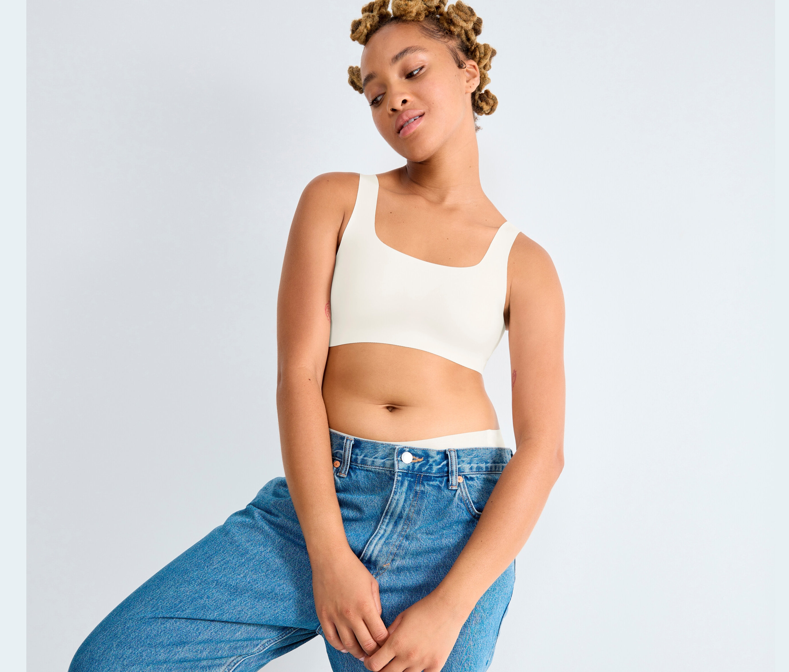 Mladá žena pózuje v džínových kalhotách a topu Sloggi ZERO Feel 2.0 v hedvábně bílé barvě.