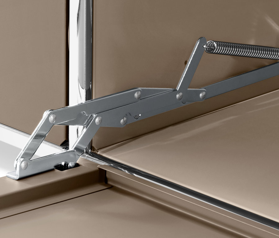 Detail stříbrného mechanismu s pružinou na hnědém povrchu.