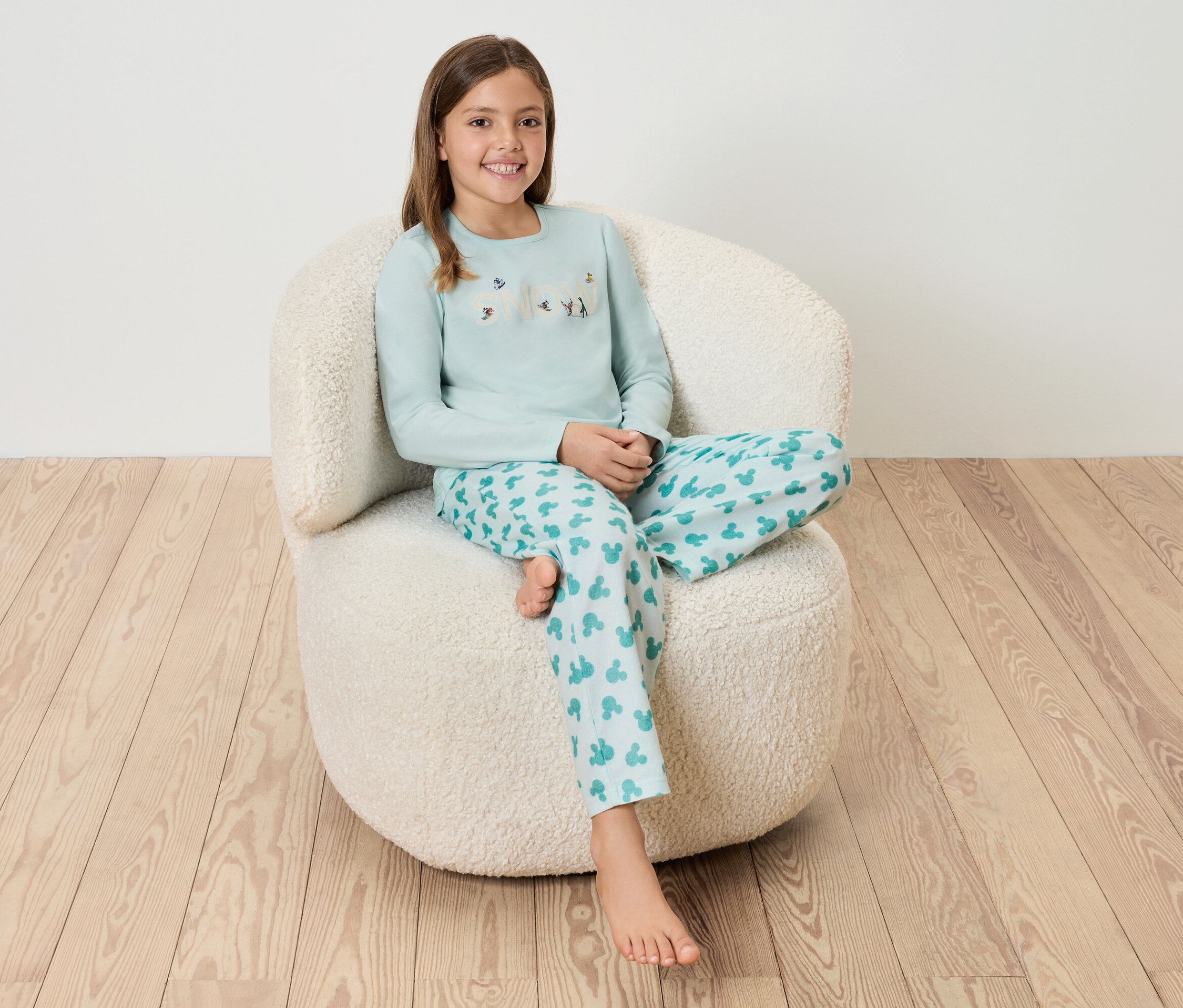 Dívka sedí v modrém pyžamu na bílém chlupatém křesle.