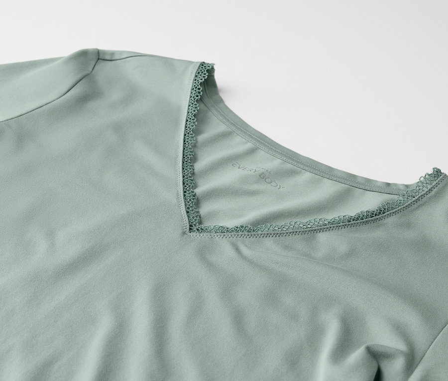 Detail světle zeleného trička s krátkým rukávem a výstřihem do V lemovaným krajkou.