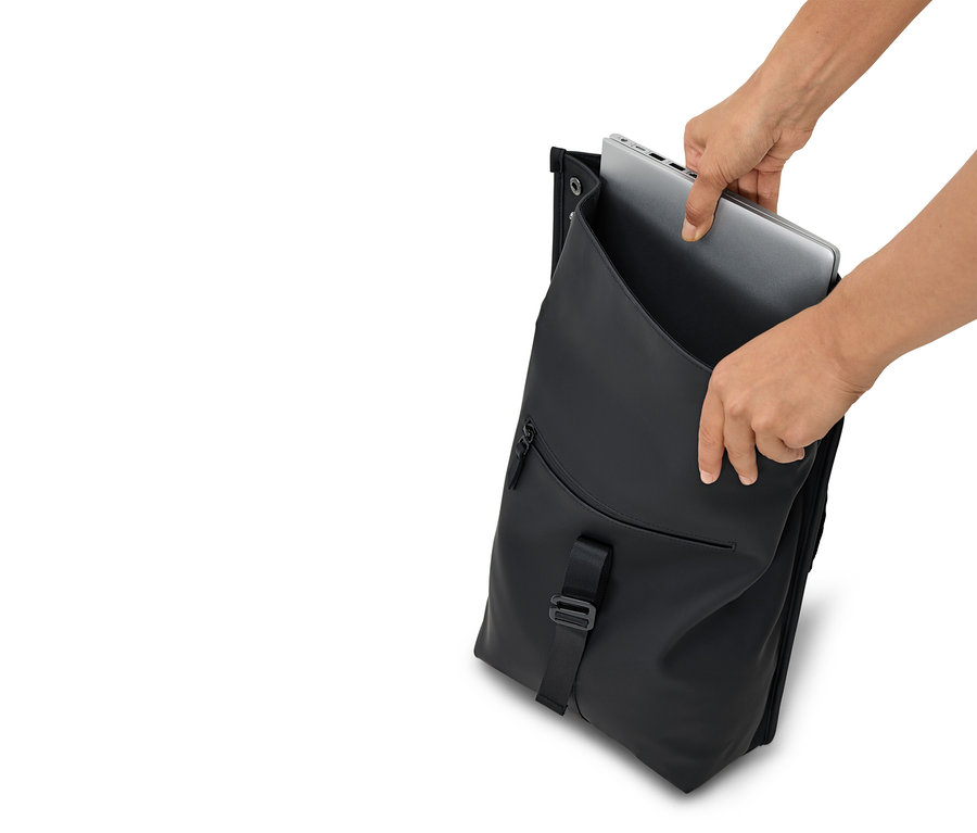 Ruce vkládají stříbrný notebook do otevřeného černého batohu.