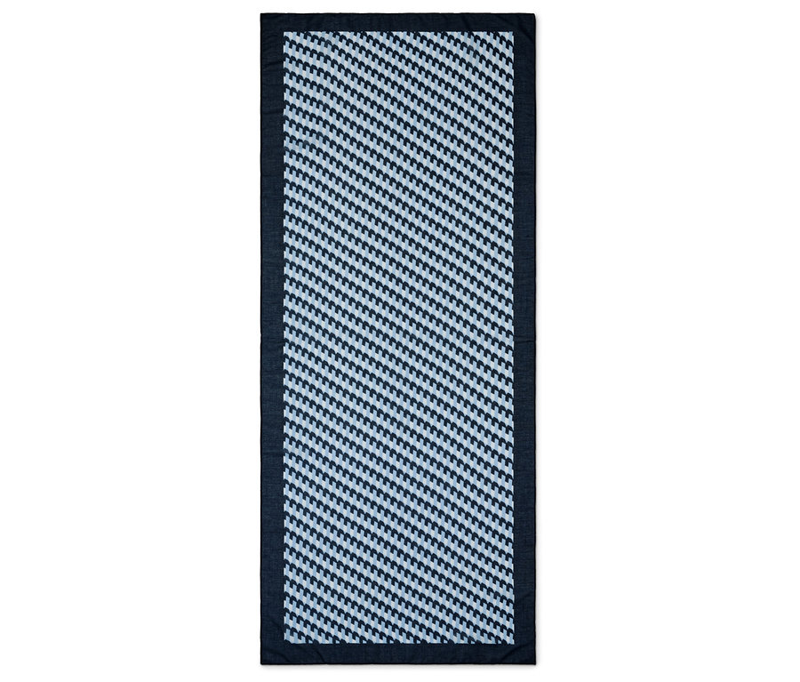Obdélníkový koberec s geometrickým vzorem v modré a bílé barvě, lemovaný tmavě modrým okrajem.