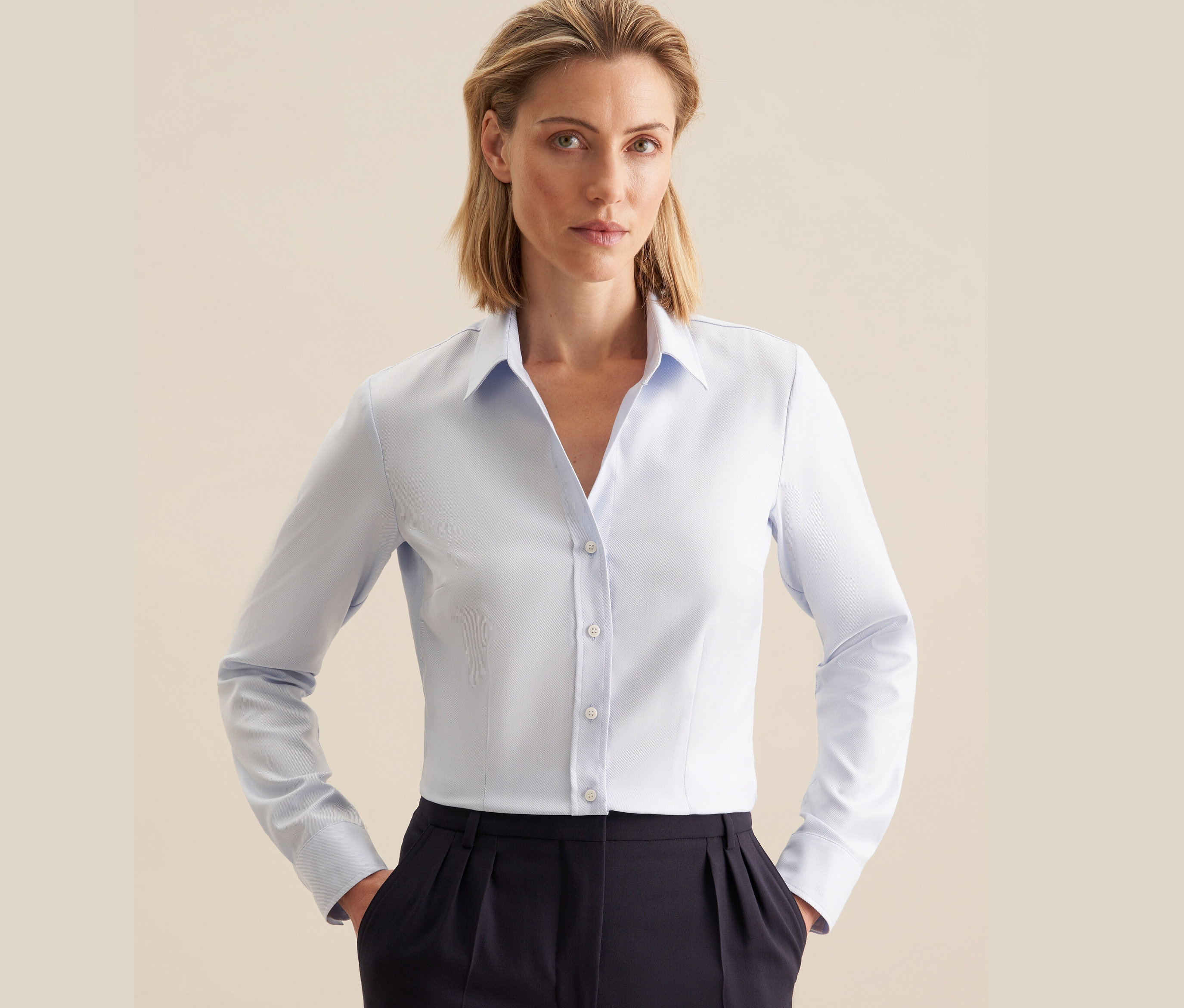 Žena má na sobě světle modrou keprovou halenku Seidensticker a tmavě modré kalhoty.