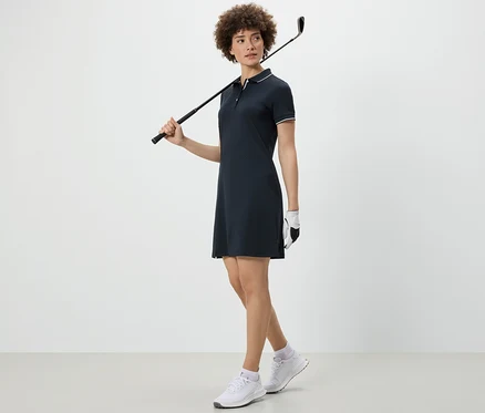 Žena drží golfovou hůl přes rameno a má na sobě sportovní šaty.