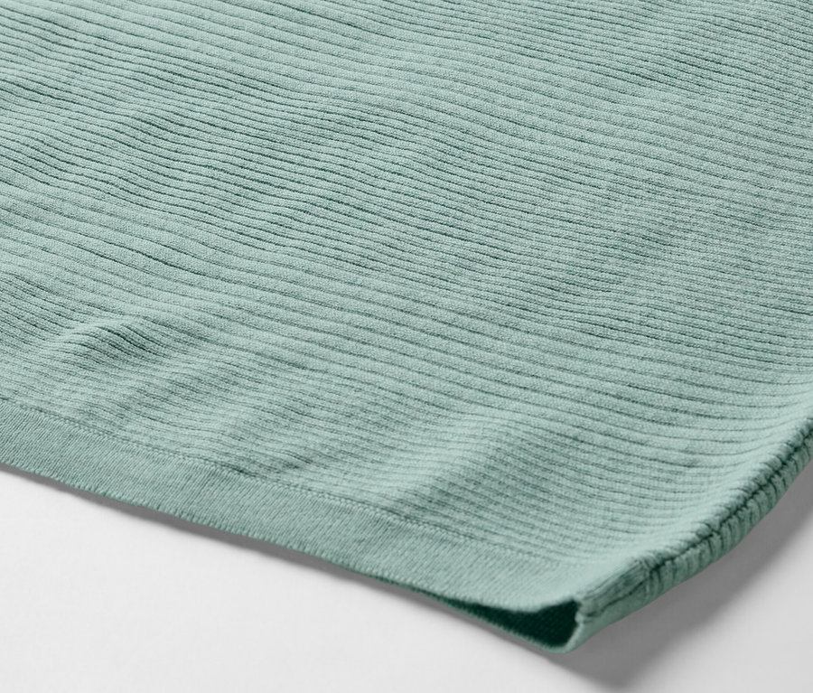 Detailní záběr na světle zelený svetr z jemného úpletu.