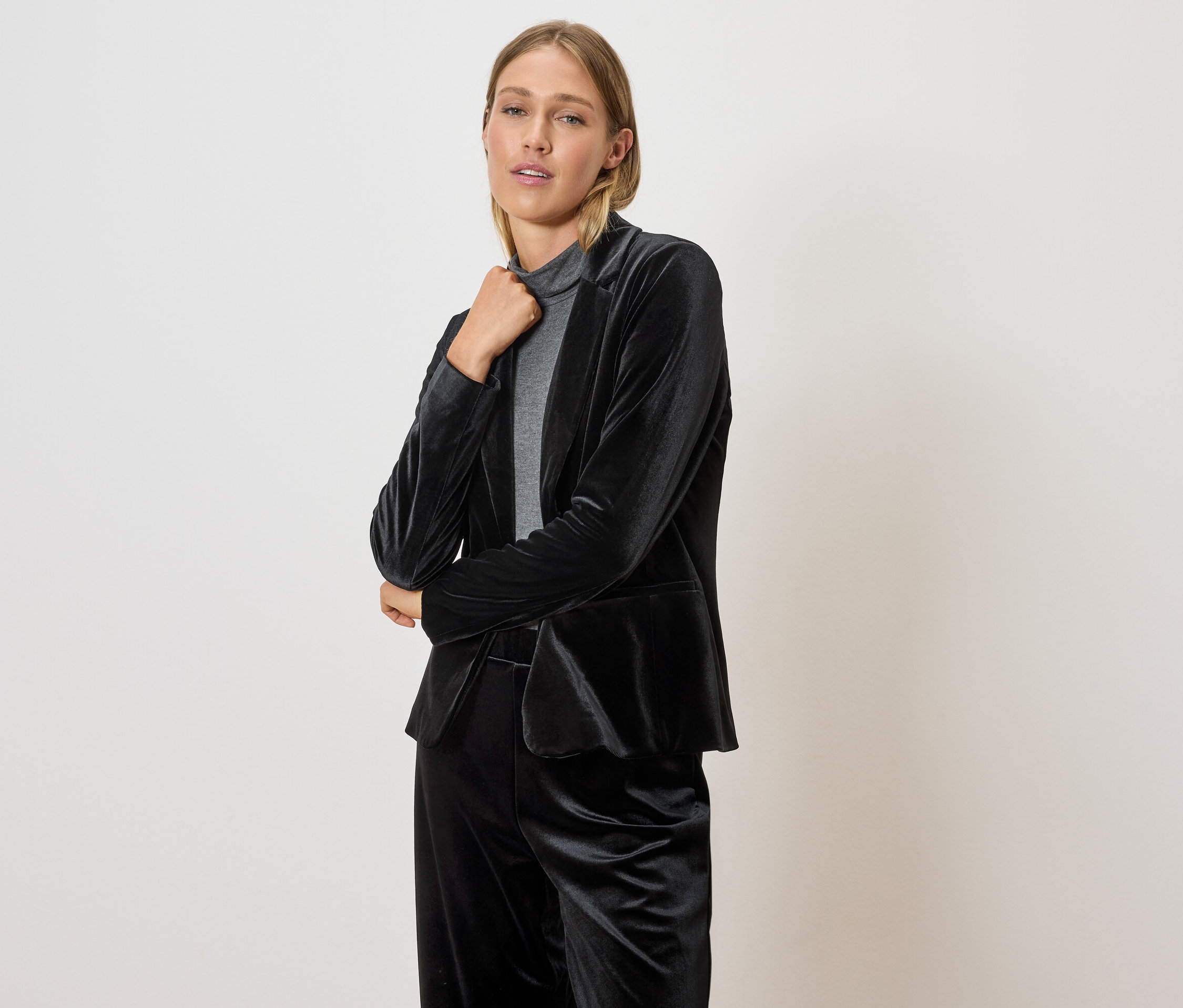 Žena pózuje v černém sametovém saku a kalhotách.