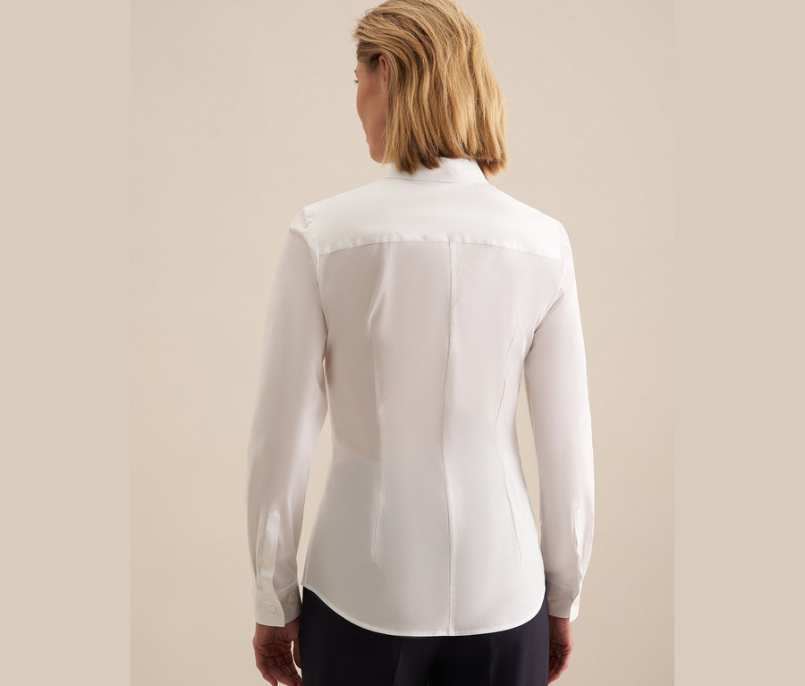 Zezadu pohled na ženu s krátkými blond vlasy v bílé halence slim fit Seidensticker a tmavě modrých kalhotách.