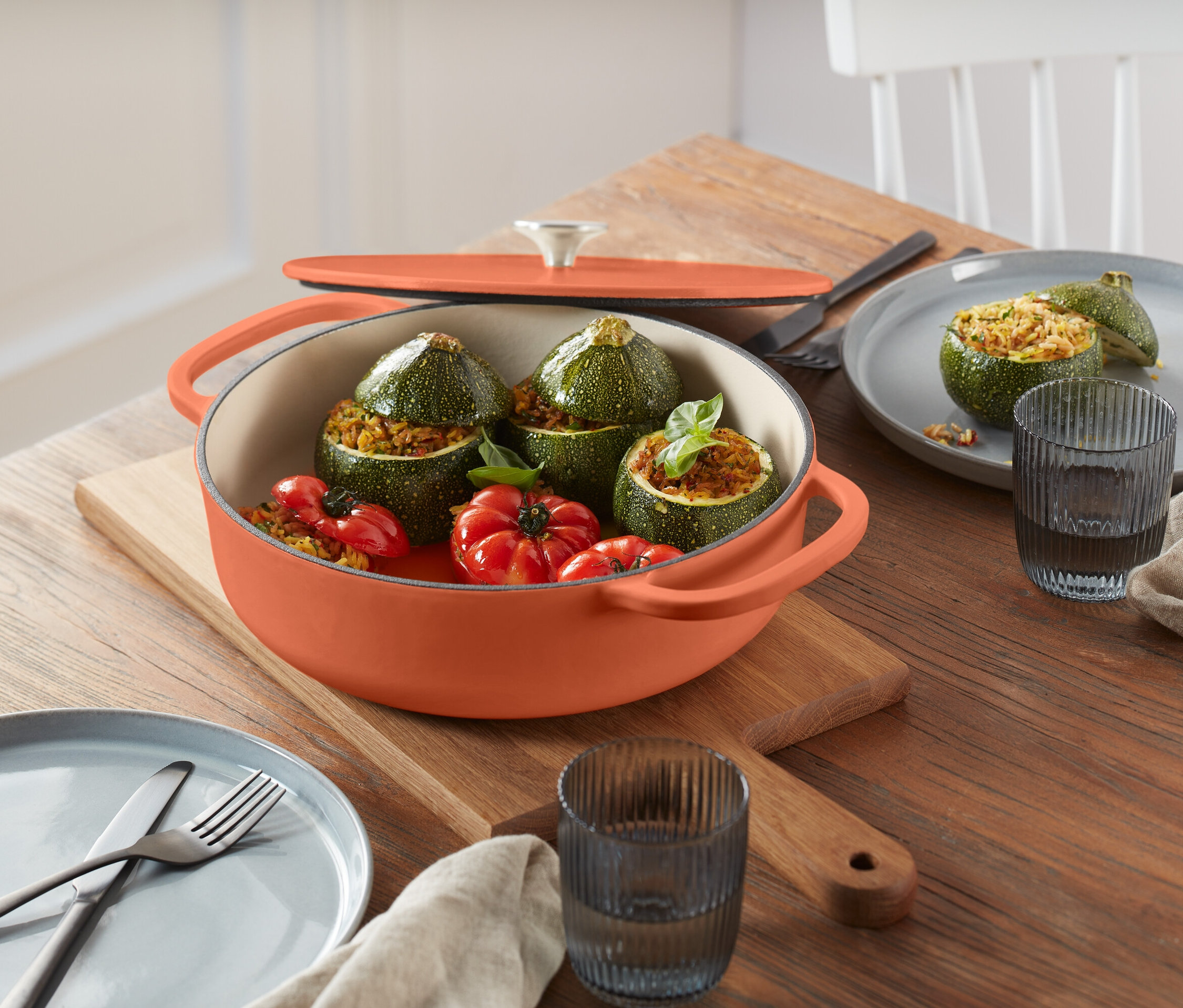 Plněné cukety a rajčata v oranžovém hrnci na dřevěném prkénku.