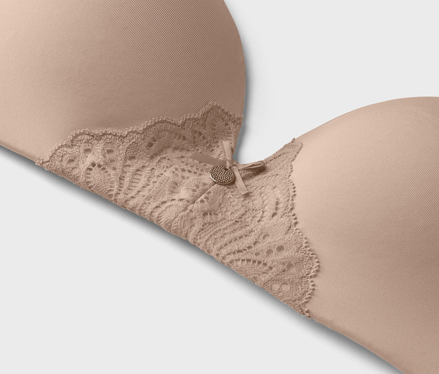 Detailní záběr béžové podprsenky s krajkovým lemem a malým ozdobným knoflíkem.