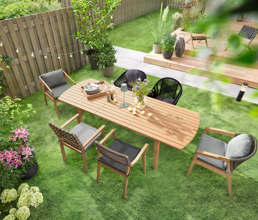 Rozkládací zahradní stůl se zaoblenými čely stojí na zeleném trávníku a je obklopený několika zahradními židlemi. Nad stolem visí solární světelný řetěz »Žárovky« a na něm stojí venkovní dobíjecí stolní lampa LED, šalvějová. Na stole je rozmístěno několik LED venkovních dobíjecích čajových svíček, 6 ks.