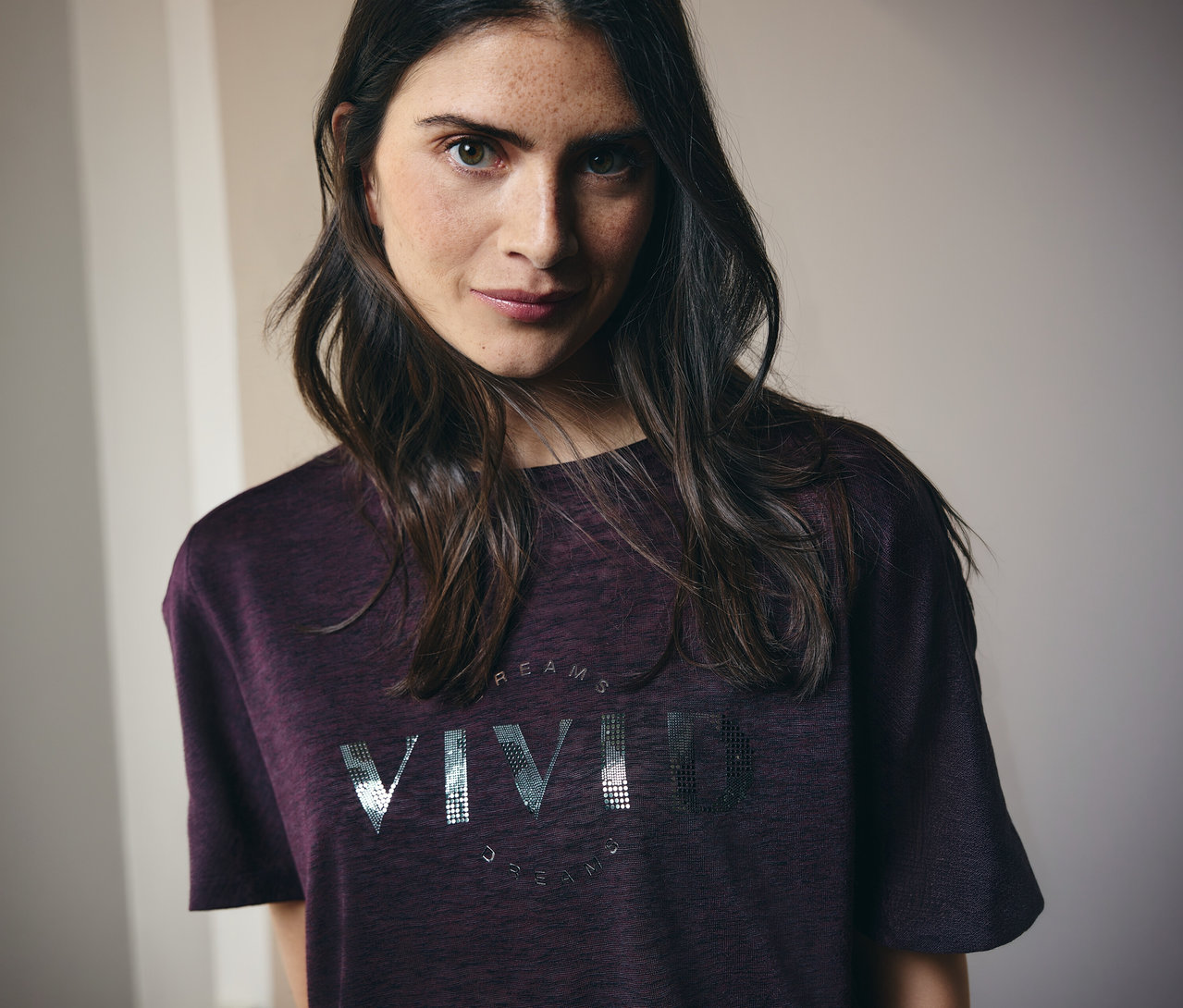 Žena s dlouhými hnědými vlasy má na sobě kaštanové tričko s nápisem "Vivid Dreams".