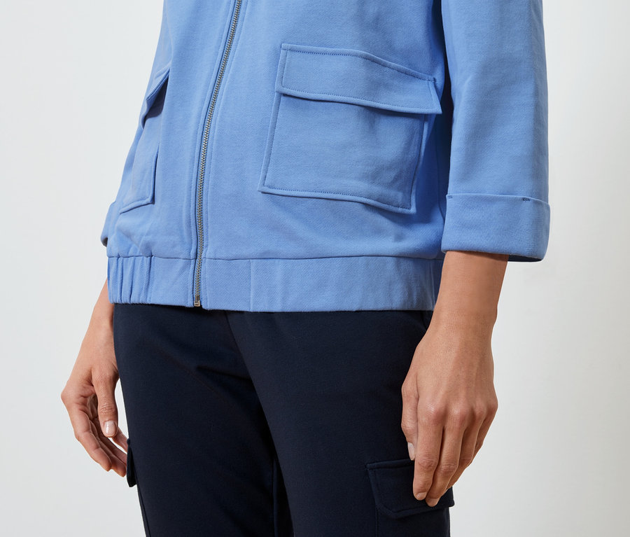 Žena má na sobě světle modrou bundu a tmavě modré kalhoty.