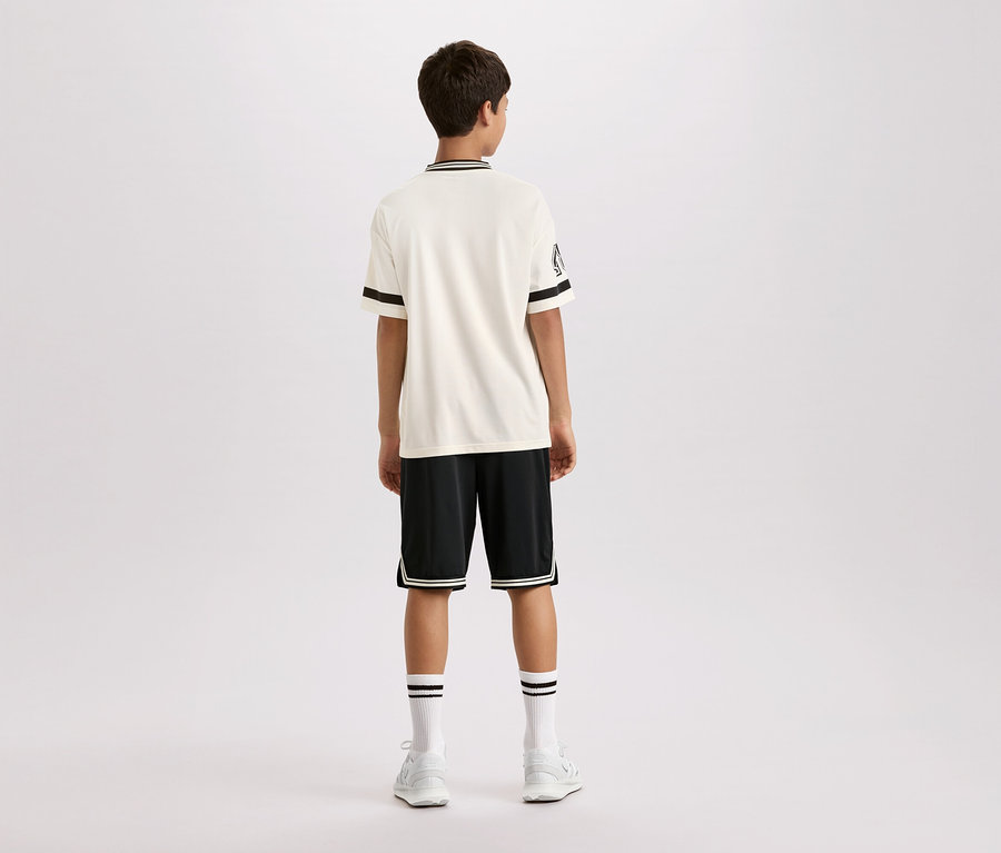 Pohled zezadu na mladého muže v krémovém tričku s krátkým rukávem s černými pruhy na límci a rukávech, černých šortkách s bílými pruhy a bílých ponožkách a botách.