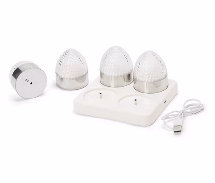 Čtyři malé kulaté lampy se stříbrnými základnami a fasetovanými, průhlednými skleněnými kopulemi stojí na bílé nabíjecí stanici s USB kabelem.