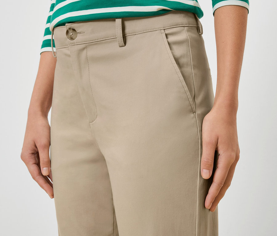 Detailní záběr ženy v béžových kalhotách a zeleno-bílém pruhovaném topu.