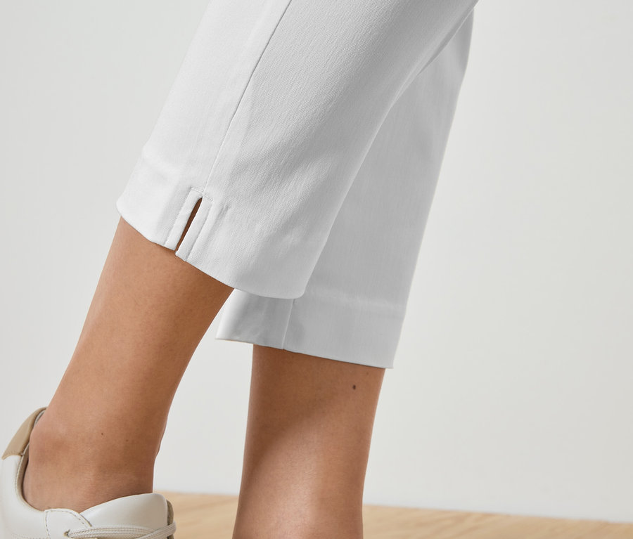 Detailní záběr na nohy osoby v bílých kalhotách a ladících teniskách.