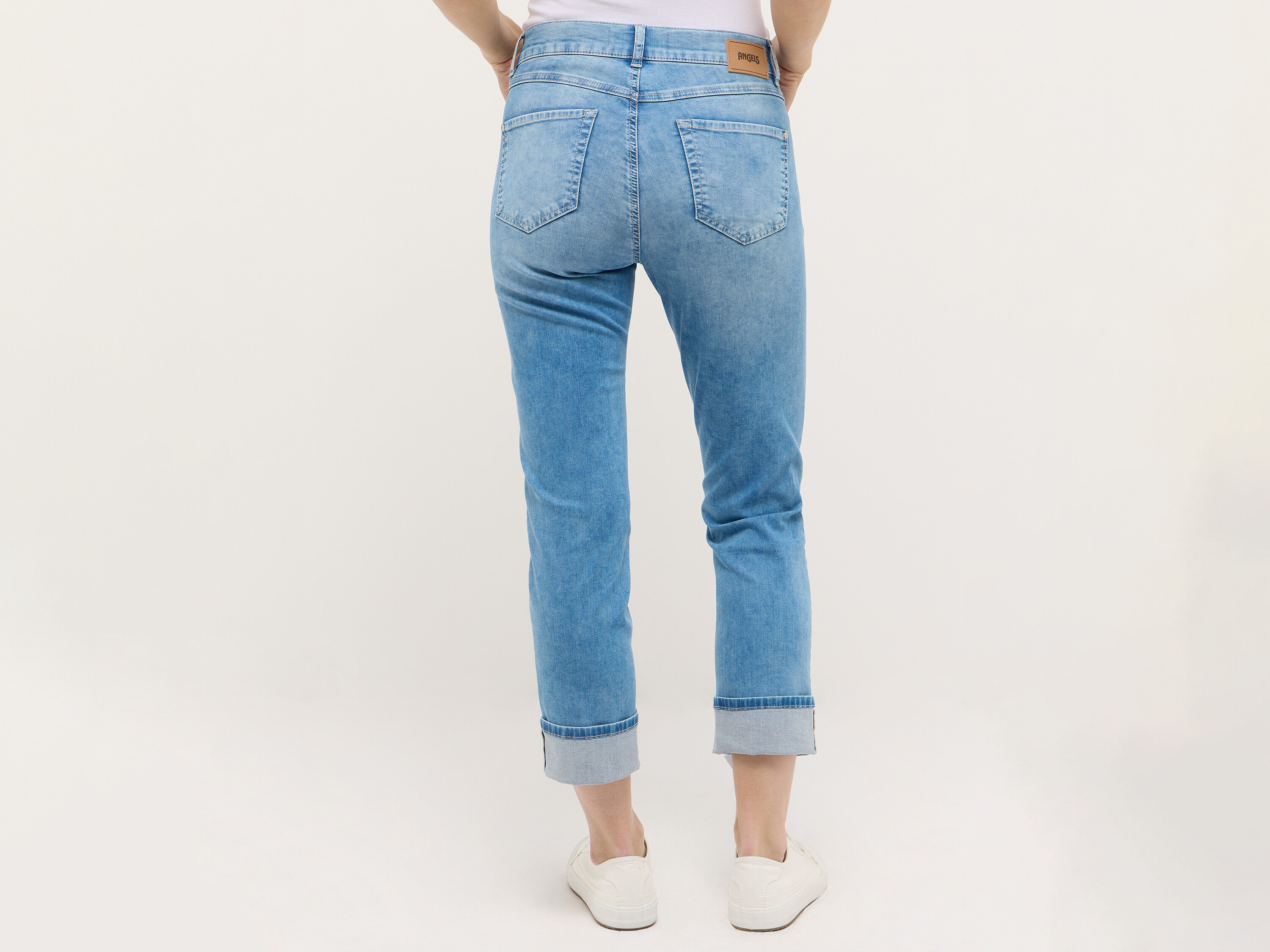 Boky a nohy ženy ve světle modrých džínách a bílých teniskách, pohled zezadu.