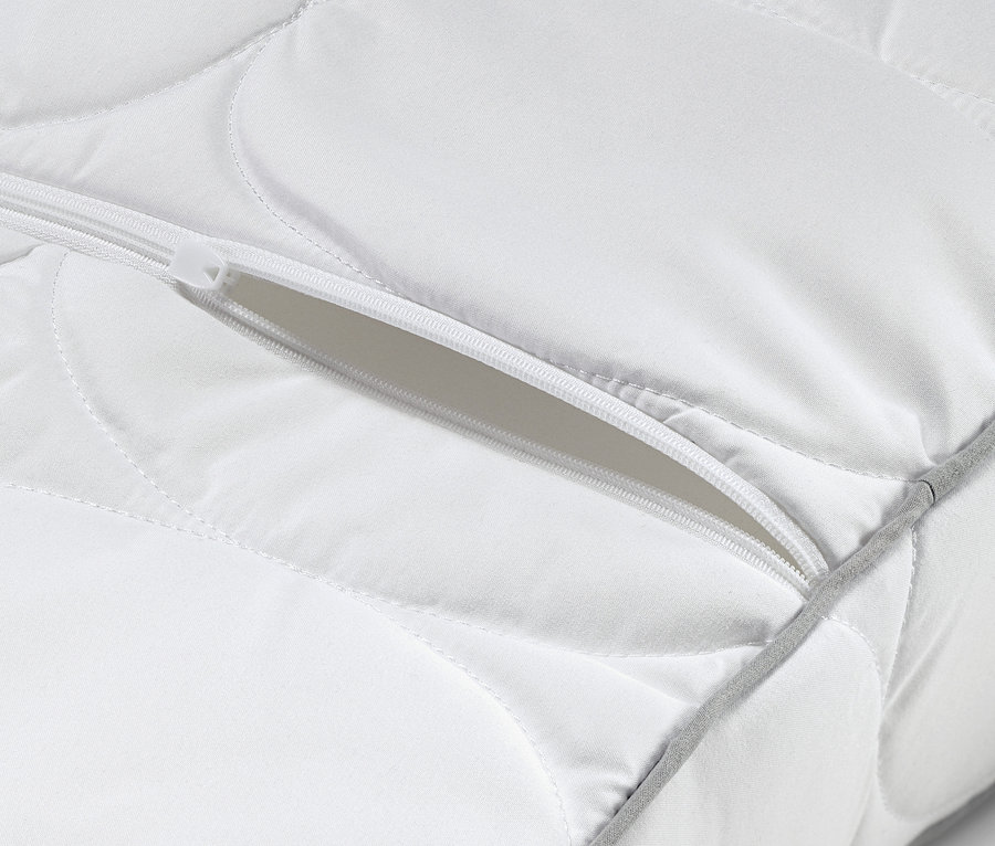 Detail bílého polštáře pro oporu krční páteře se zipem.