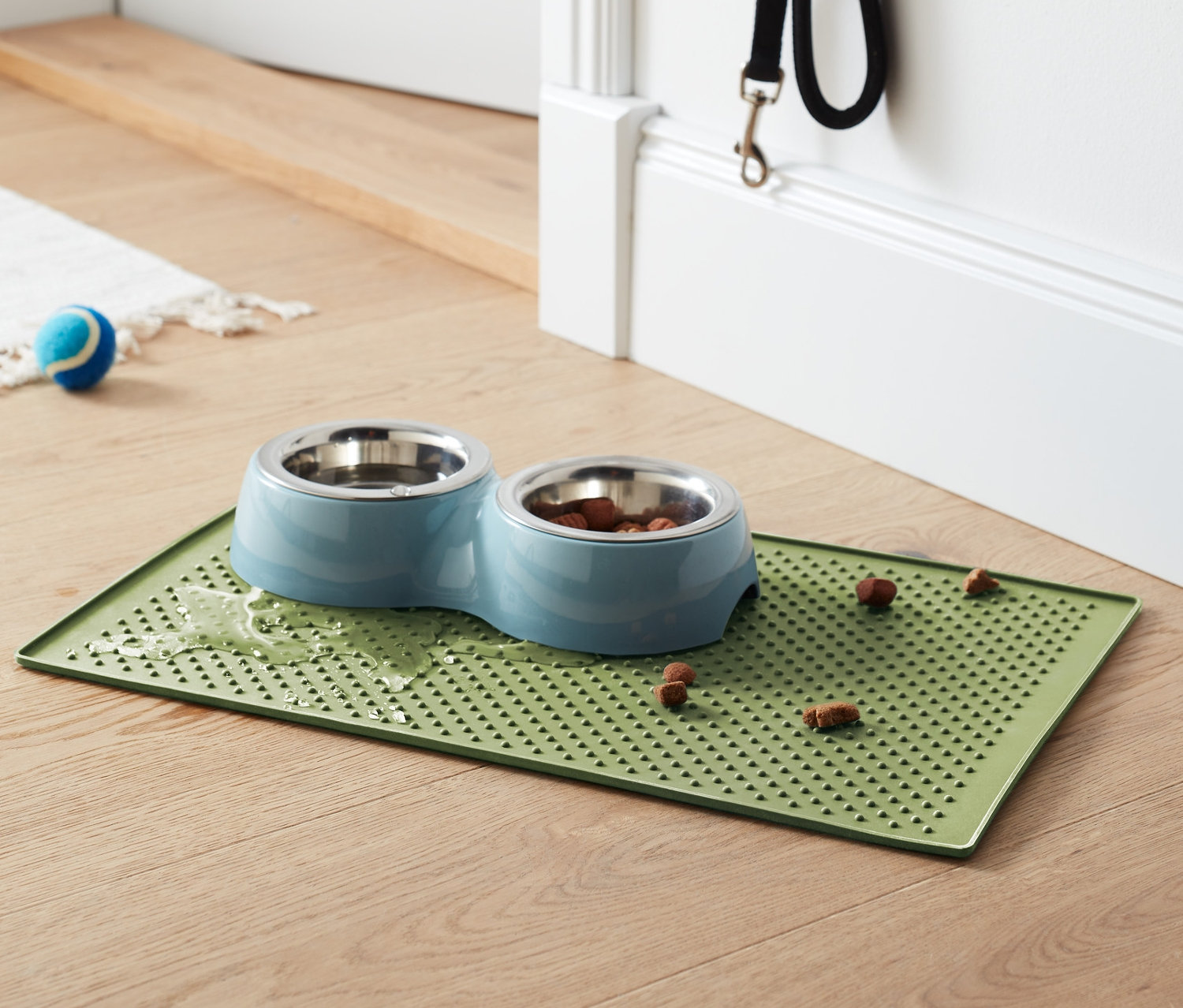 Dvojitá miska pro domácí mazlíčky s jídlem na zelené podložce pod misku na krmivo.