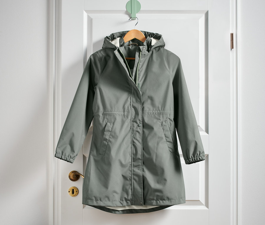 Zelená parka do deště visí na bílých dveřích.