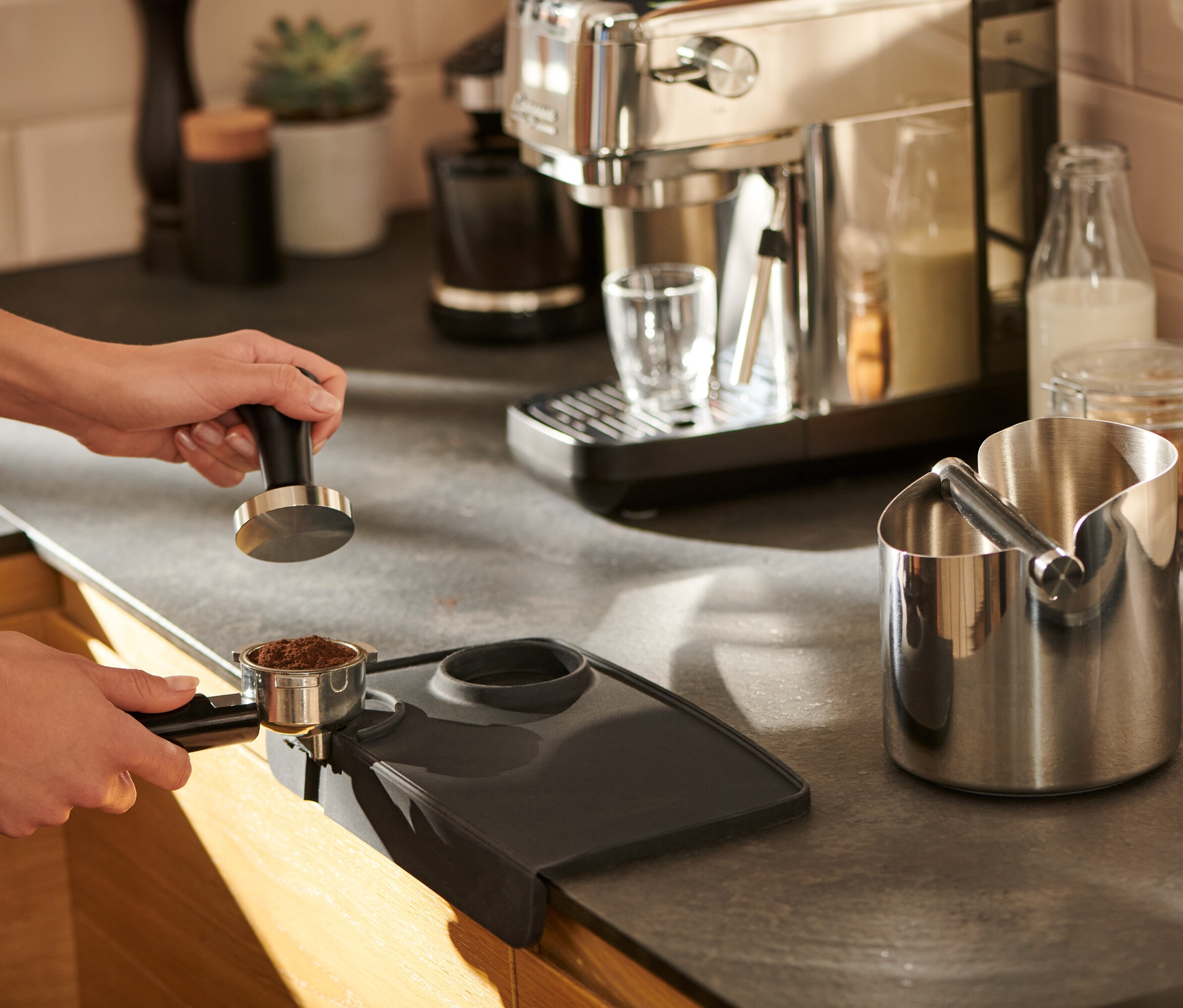 Žena pěchuje kávu na černé podložce na pěchování kávy.