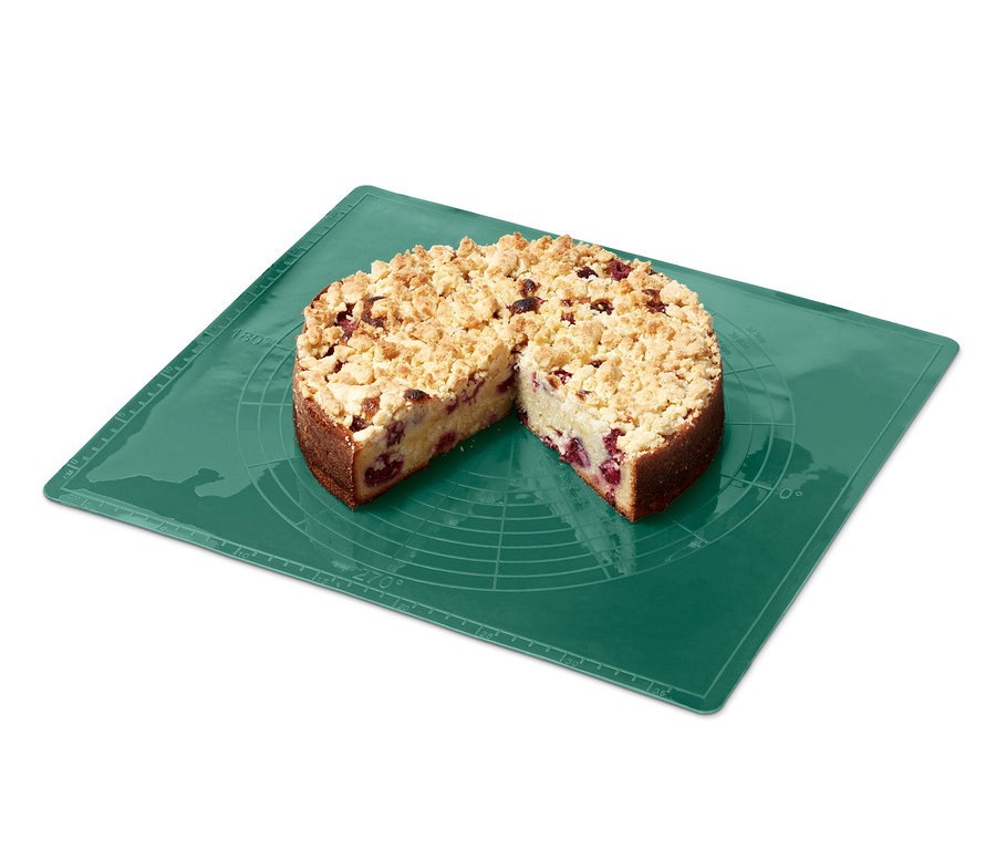 Koláč s krájenou částí na zelené opakovaně použitelné podložce na pečení.