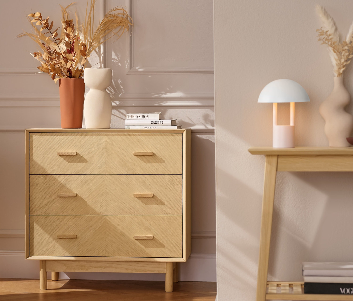 Komoda se zásuvkami z jasanového dřeva s dekorativními čely vedle šedého křesla s oranžovou dekou.