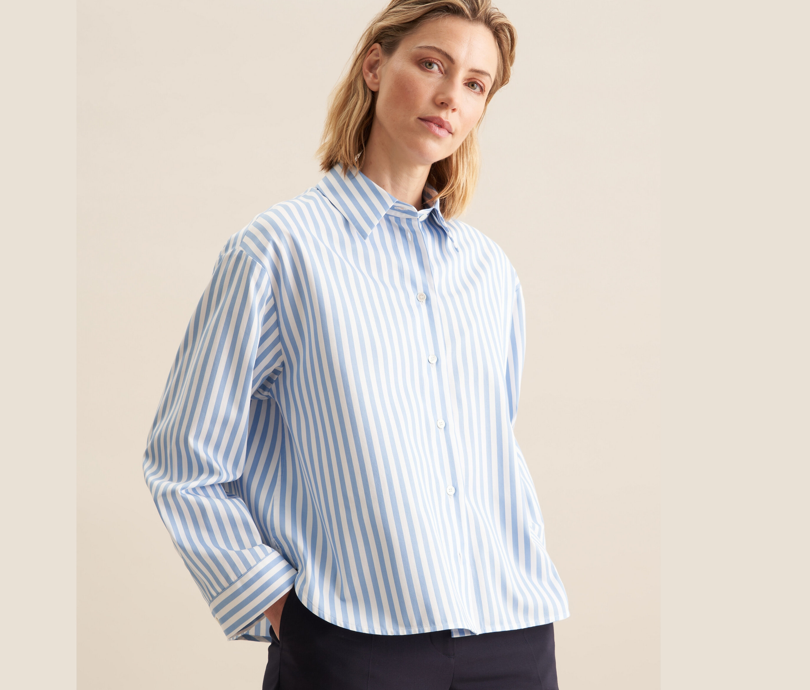 Žena má na sobě modrou košili Seidensticker oversize s bílými proužky a tmavě modré kalhoty.