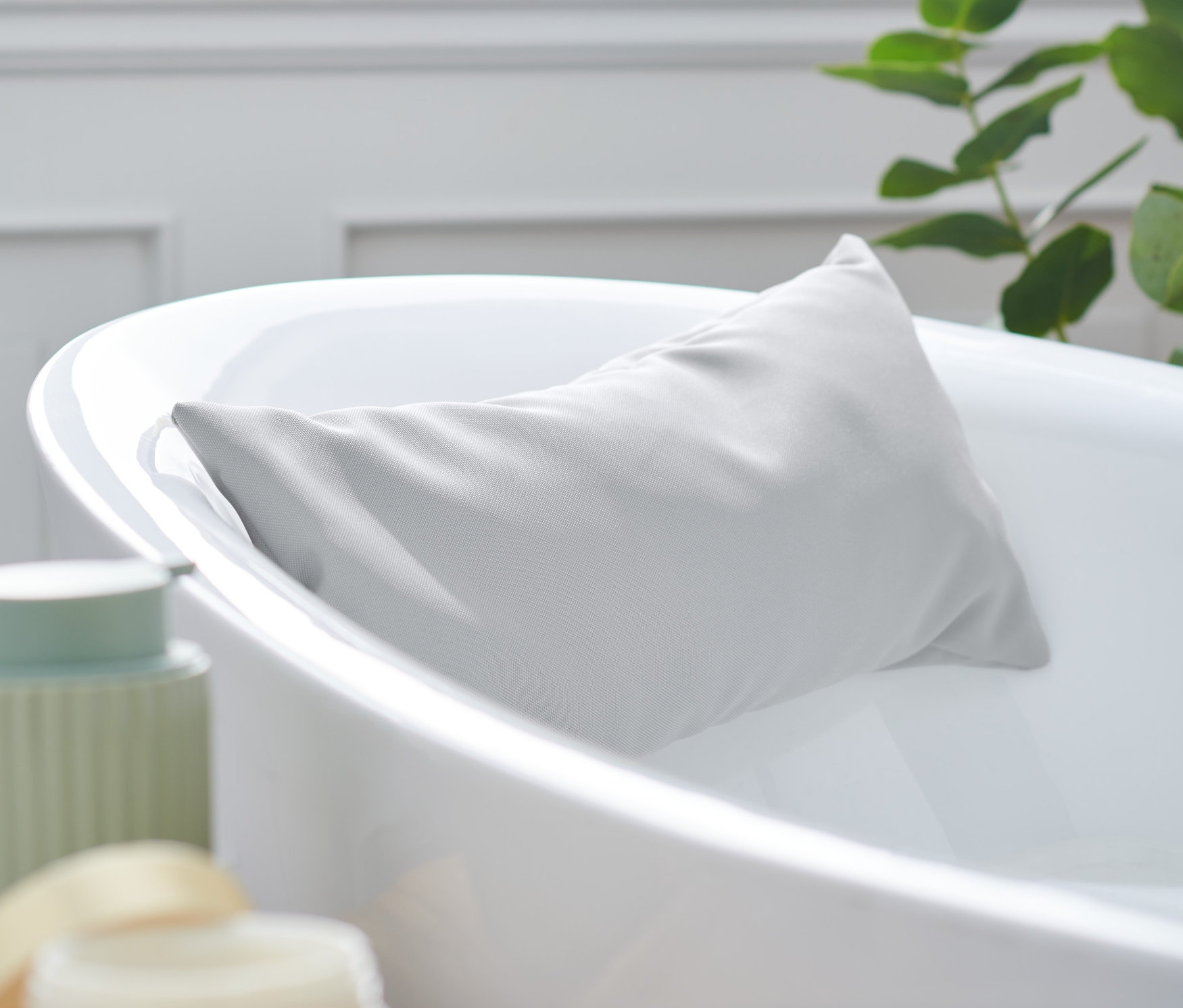 Šedý polštářek do vany je opřený o okraj bílé vany.