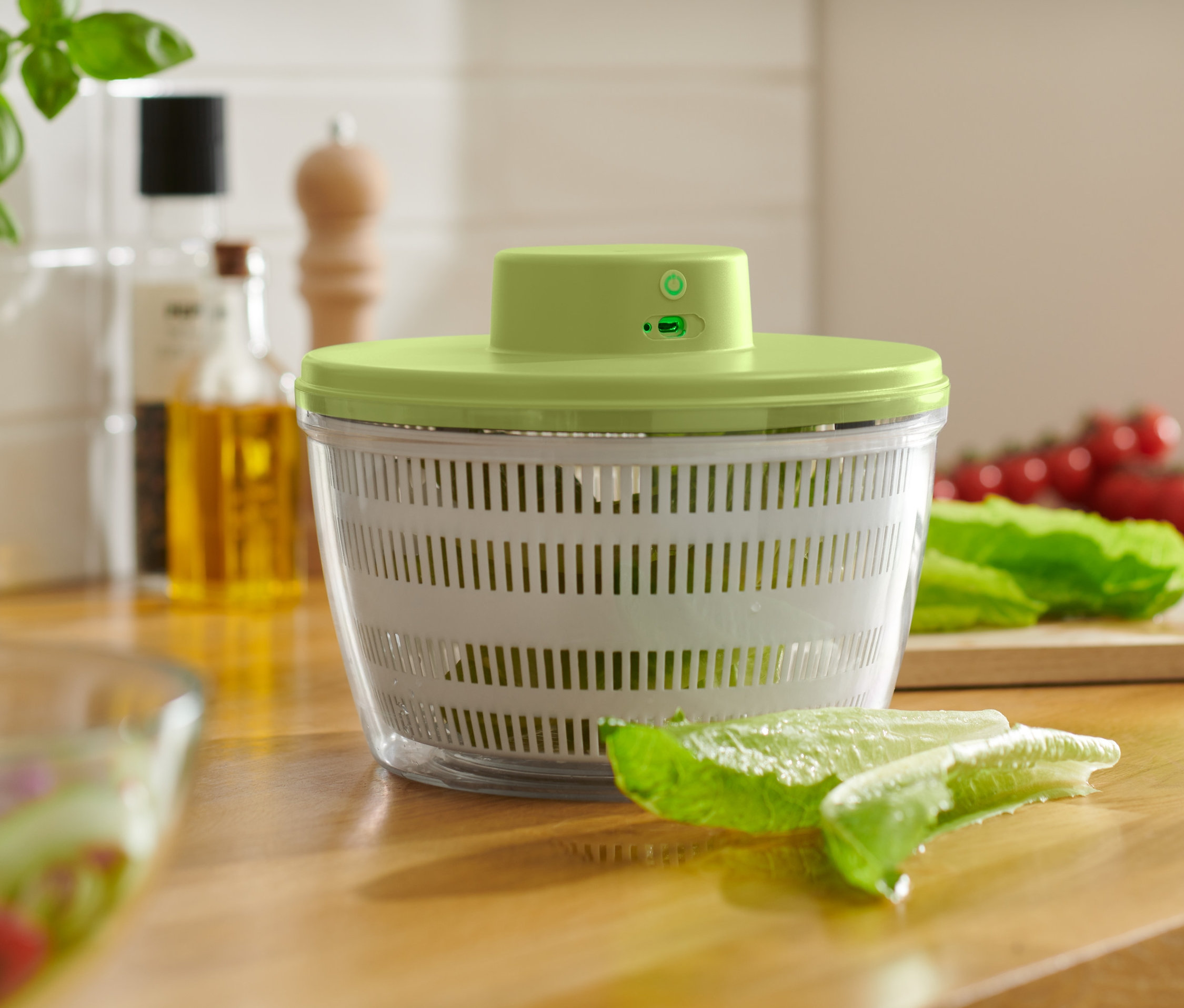 Bateriová elektrická odstředivka na saláty stojí na dřevěné desce. Vedle ní leží salát a rajčata.