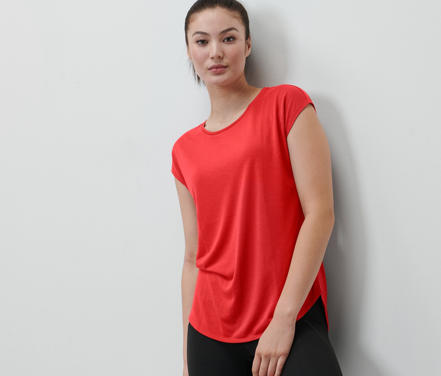 Žena opřená o zeď má na sobě červené sportovní tričko.
