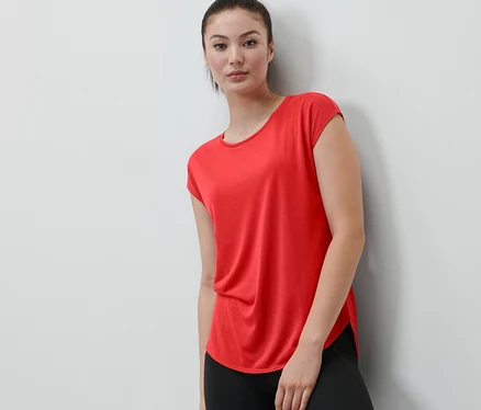 Žena opřená o zeď má na sobě červené sportovní tričko.
