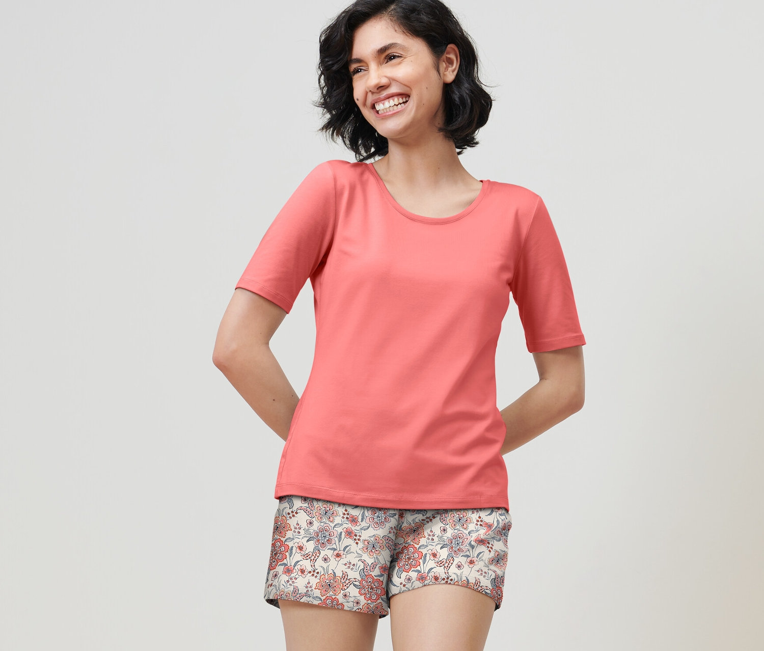 Usmívající se žena má na sobě krátké pyžamo papájové barvy.