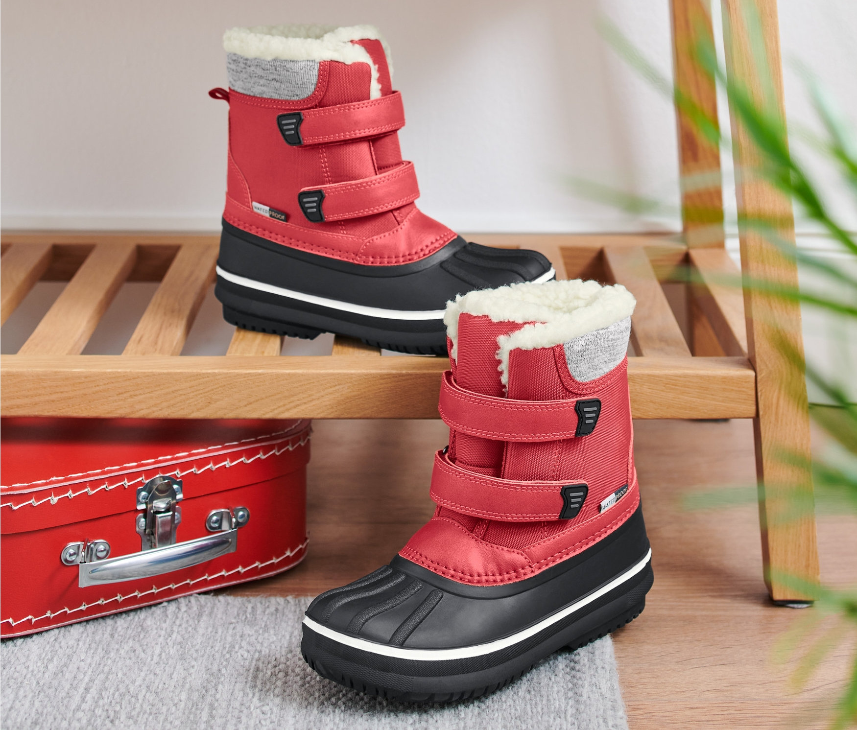 Dvoje červené dětské boty do každého počasí na dřevěné polici.