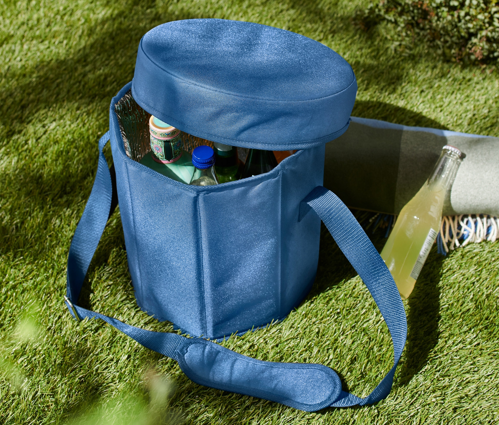 Modrá chladicí taška 2 v 1 na trávě, částečně otevřená, s lahvemi uvnitř.