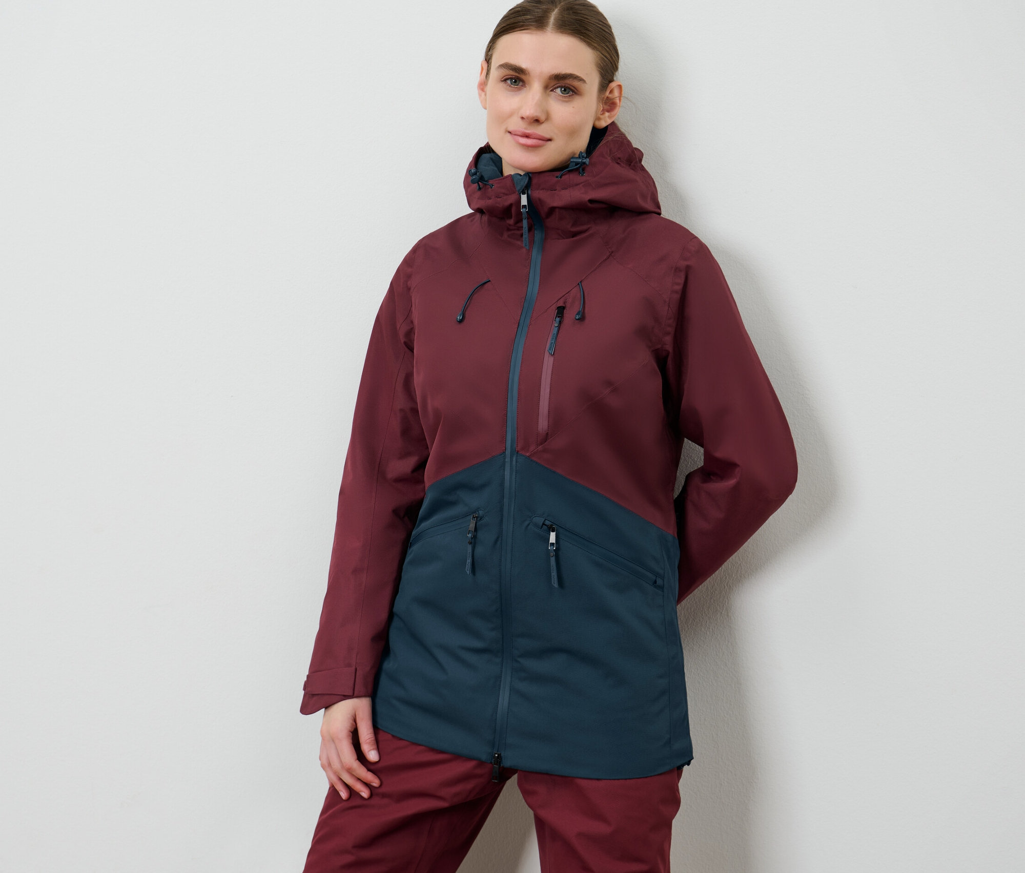 Žena pózuje v lyžařské a snowboardové bundě.