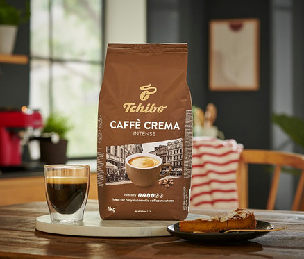 Balení zrnkové kávy Caffè Crema Intense 1 kg vedle šálku kávy a kousku koláče.