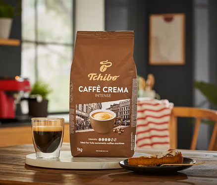 Balení zrnkové kávy Caffè Crema Intense 1 kg vedle šálku kávy a kousku koláče.
