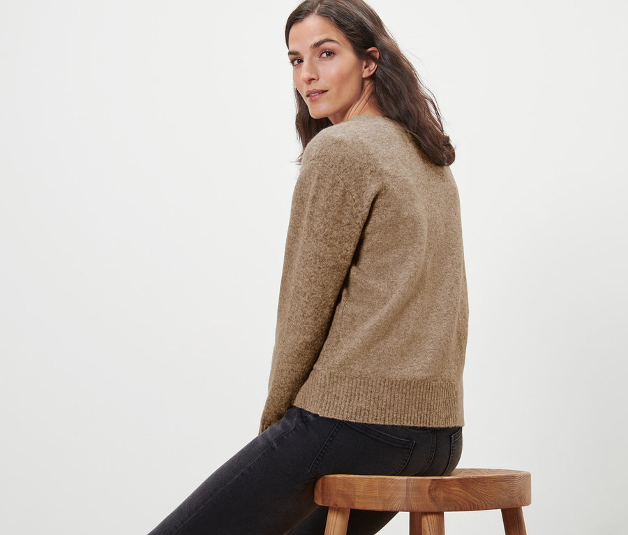 Žena sedí na dřevěné stoličce a má na sobě pletený svetr s vlnou.