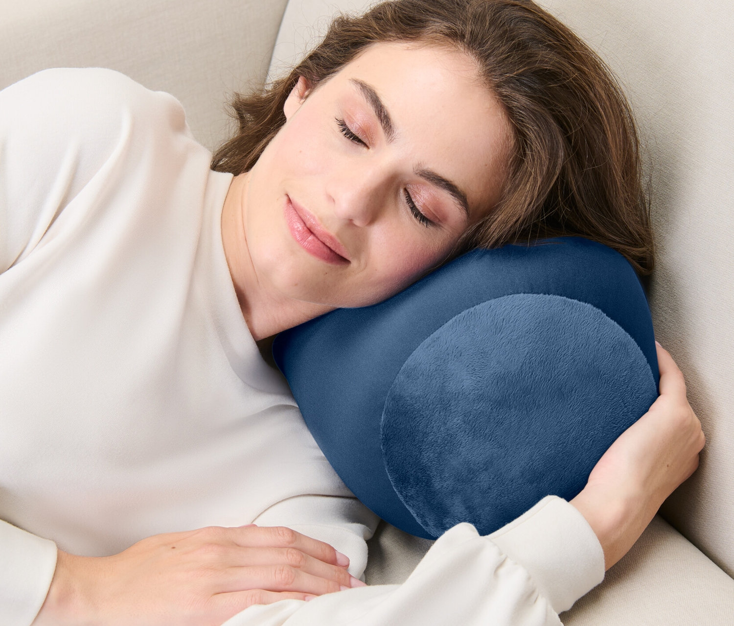 Žena spí na béžové pohovce s relaxačním polštářkem.