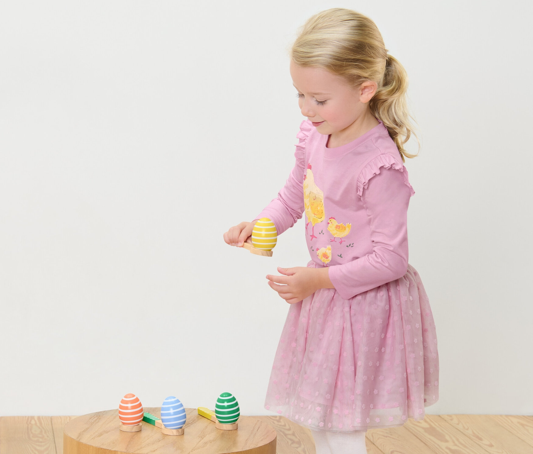 Dívka hraje Hra Vejce na lžíci. Stojí a soustředí se na vyvažování vejce na lžíci.