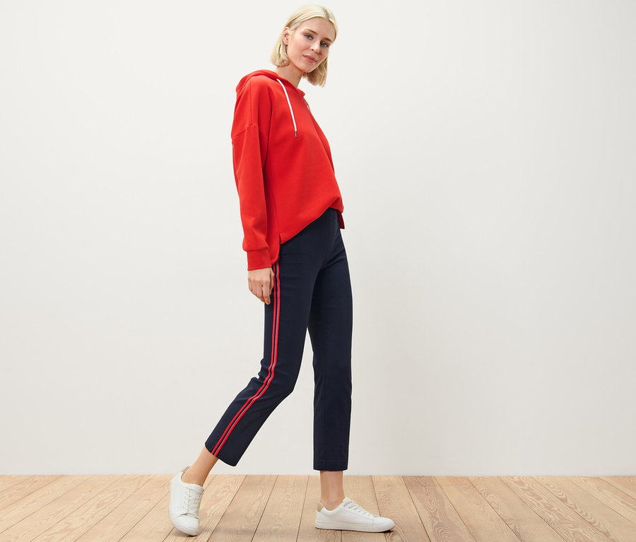 Blonďatá žena pózuje v červené mikině a strečových kalhotách s lampasovými pruhy.