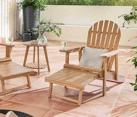 Dvojité a samostatné relaxační křeslo Adirondack s výsuvnou podnožkou stojí na terase s venkovními polštáři s lněným omakem.