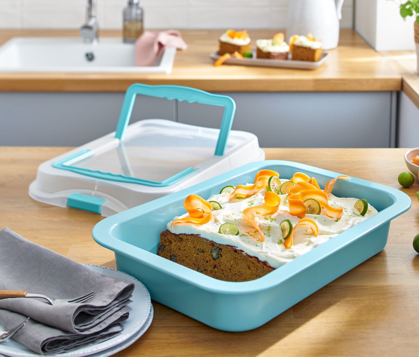 Plech na pečení s víkem a upečený koláč s polevou a ozdobami z mrkve a limetky na dřevěném stole.