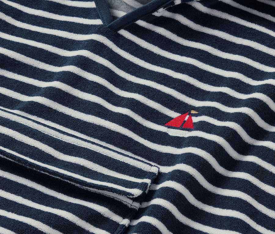 Detail froté ponča s námořnickým motivem s modrými a bílými pruhy a malou červenou výšivkou plachetnice.