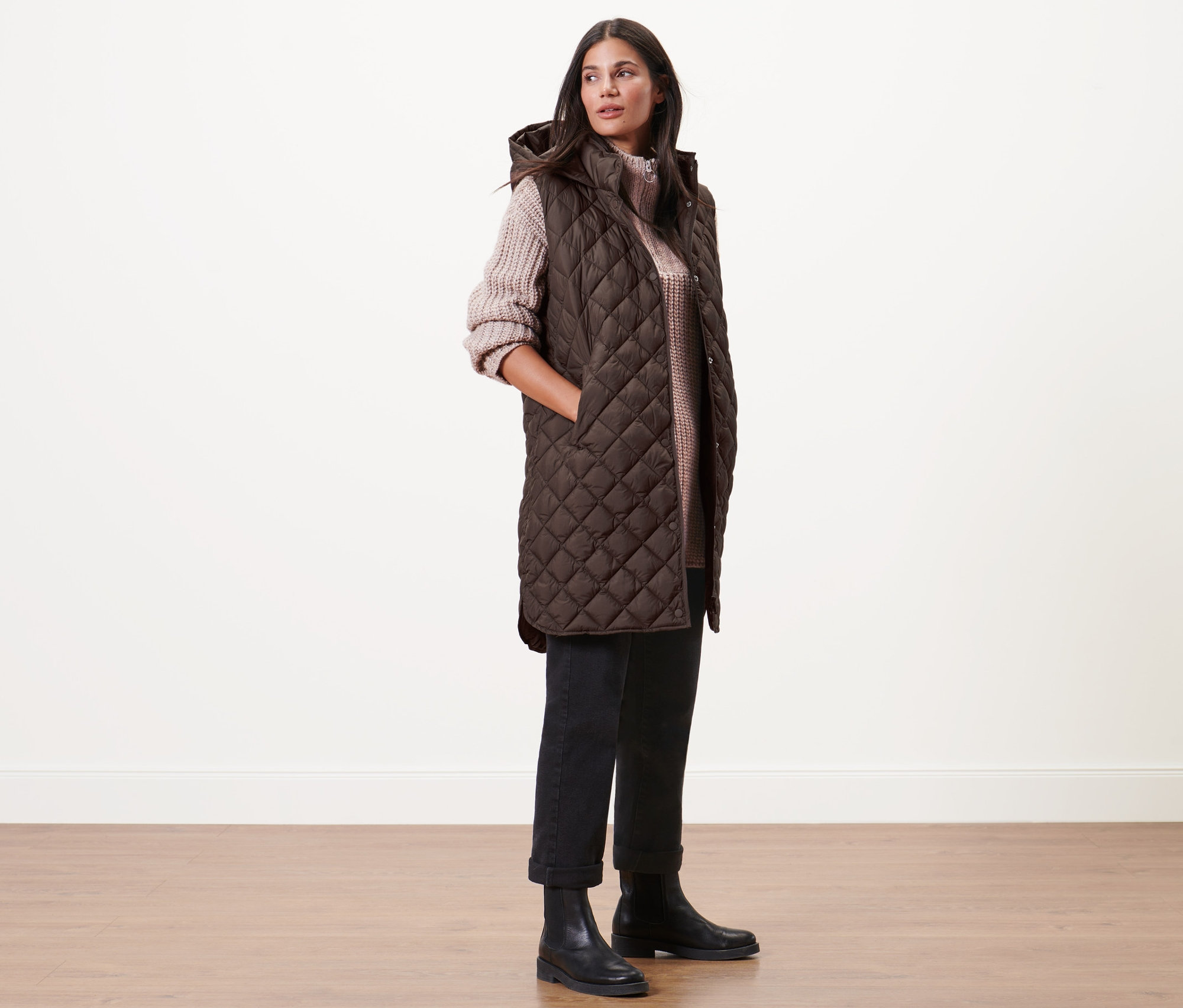 Žena pózuje v dlouhé prošívané vestě s kapucí.